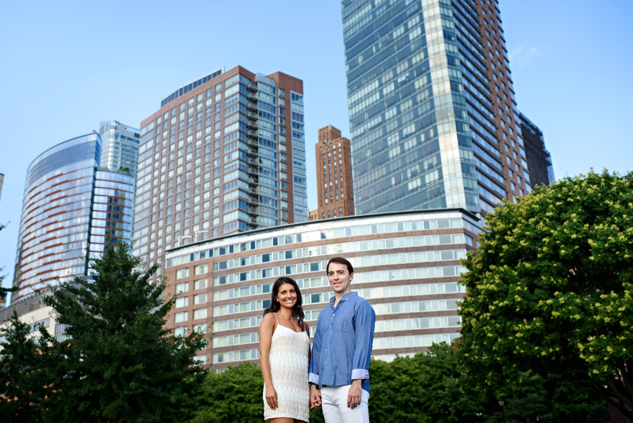 A cute couple hold hands with the manhattan city skyline behind them during their battery park engagement session.